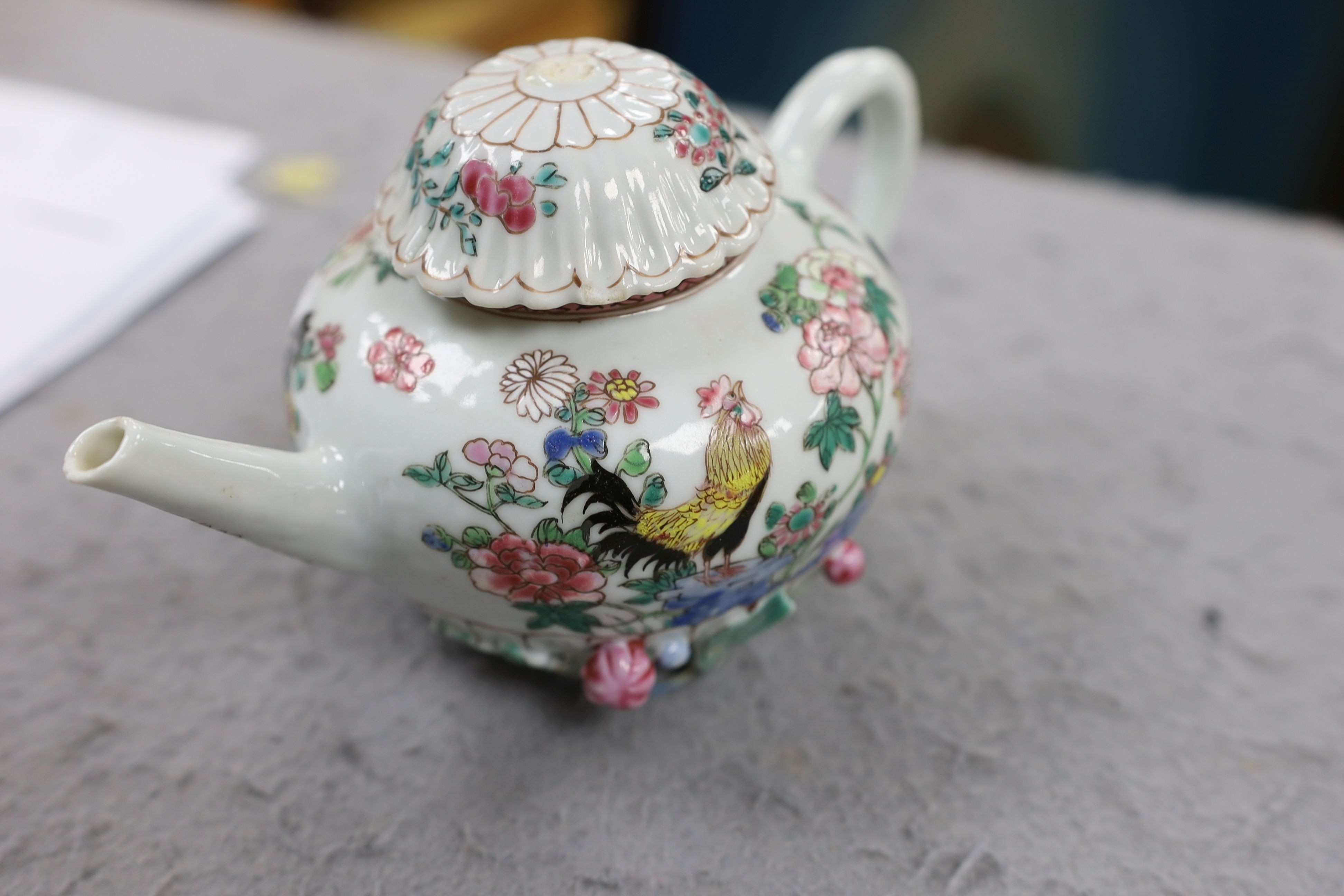 A Chinese famille rose chrysanthemum moulded teapot, early Qianlong period, painted with a cockerel amongst flowers, on a cage work base, 10 cms high